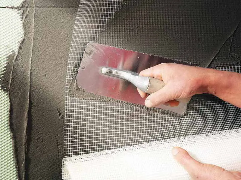 Trowel pressing fibreglass reinforcing mesh into fresh plaster on a wall
